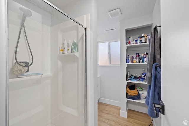 full bath with a shower stall, visible vents, baseboards, and wood finished floors