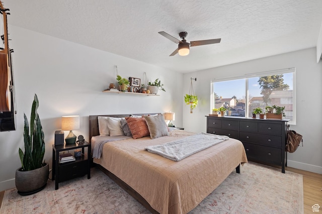 bedroom with a ceiling fan, light wood-type flooring, a textured ceiling, and baseboards