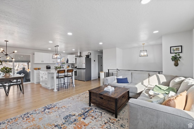 living room with a chandelier, a textured ceiling, light wood-type flooring, and recessed lighting