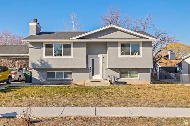 raised ranch with a carport, a front lawn, a chimney, and stucco siding