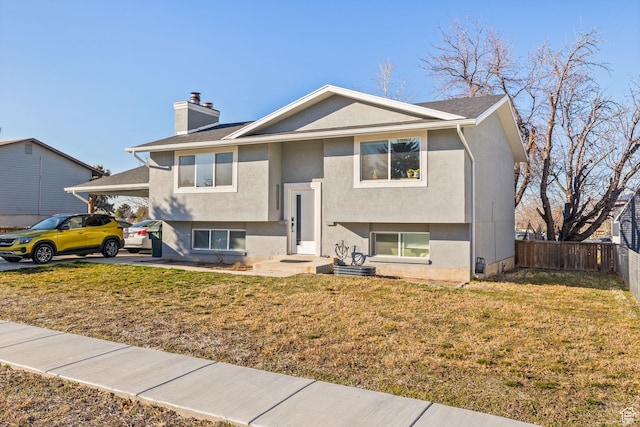 raised ranch with a chimney, fence, an attached carport, and stucco siding