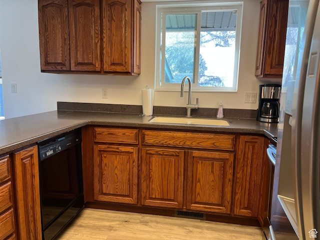 kitchen featuring a sink, light wood-type flooring, freestanding refrigerator, dishwasher, and dark countertops