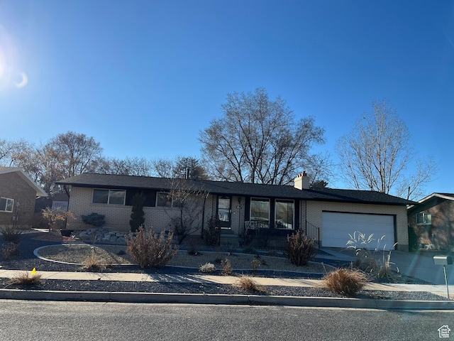 ranch-style house with concrete driveway, brick siding, a chimney, and an attached garage