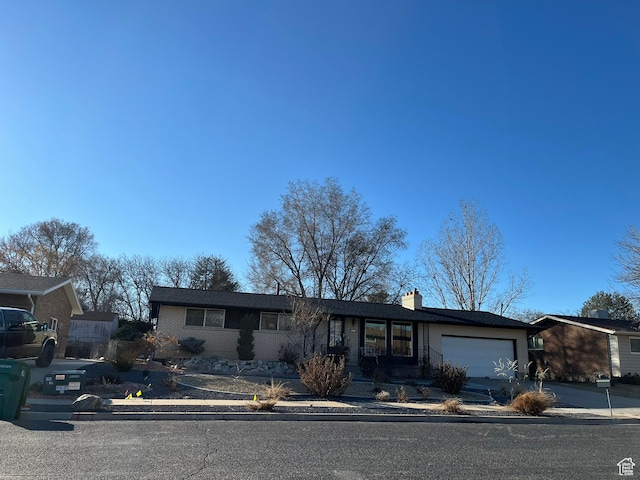 view of front of home featuring driveway, brick siding, a chimney, and an attached garage