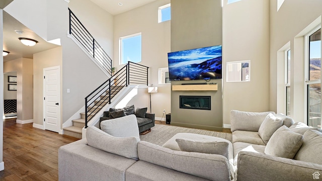 living area with stairway, wood finished floors, a glass covered fireplace, a towering ceiling, and baseboards