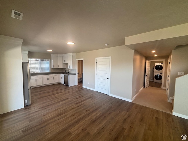 kitchen featuring stacked washer / drying machine, white cabinets, stainless steel appliances, dark countertops, and dark wood-type flooring