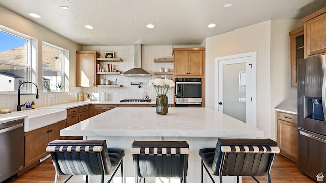 kitchen featuring wall chimney exhaust hood, a sink, backsplash, open shelves, and appliances with stainless steel finishes