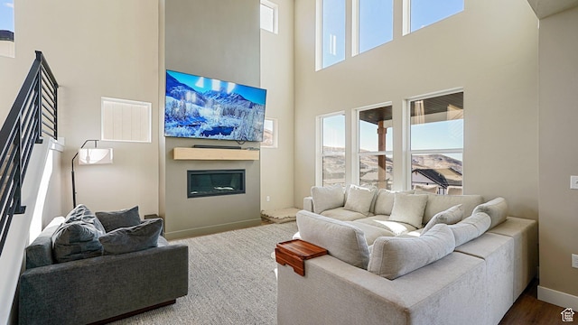 living area featuring a glass covered fireplace, plenty of natural light, a high ceiling, and baseboards
