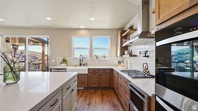 kitchen featuring wall chimney range hood, wood finished floors, a sink, stainless steel gas stovetop, and recessed lighting