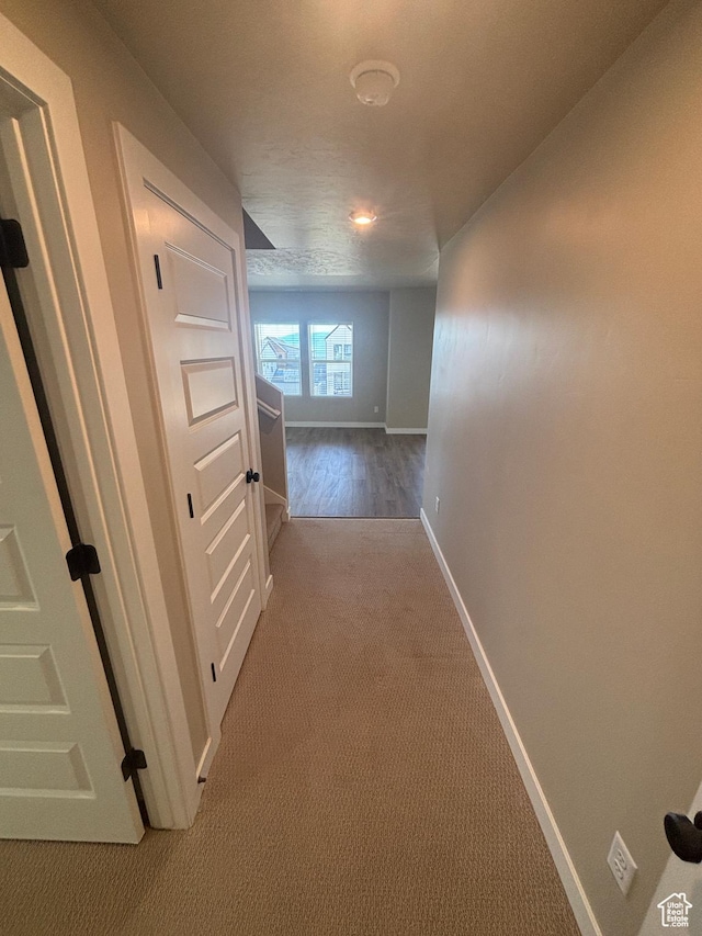 corridor featuring baseboards and light carpet