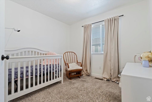 carpeted bedroom featuring a crib and baseboards