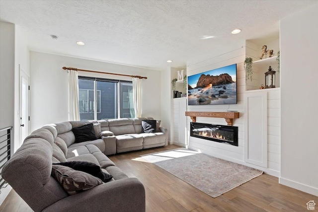 living room with recessed lighting, a glass covered fireplace, a textured ceiling, wood finished floors, and baseboards