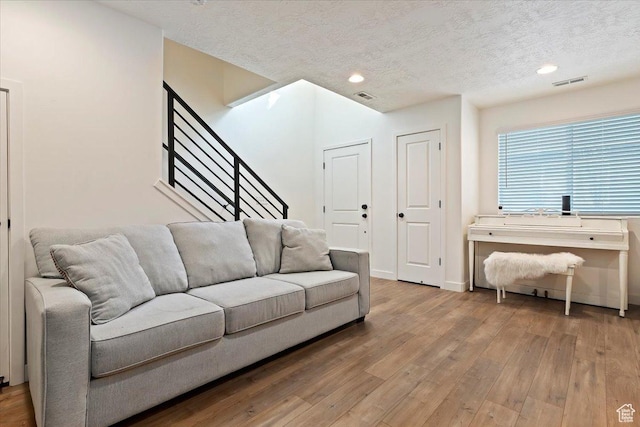 living room with a textured ceiling, stairs, visible vents, and wood finished floors