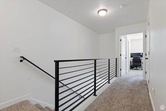 hallway featuring carpet, baseboards, a textured ceiling, and an upstairs landing
