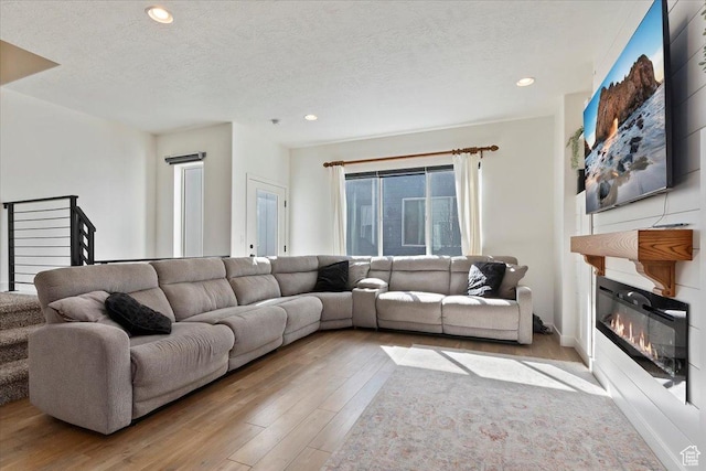 living area with a glass covered fireplace, a textured ceiling, recessed lighting, and wood finished floors