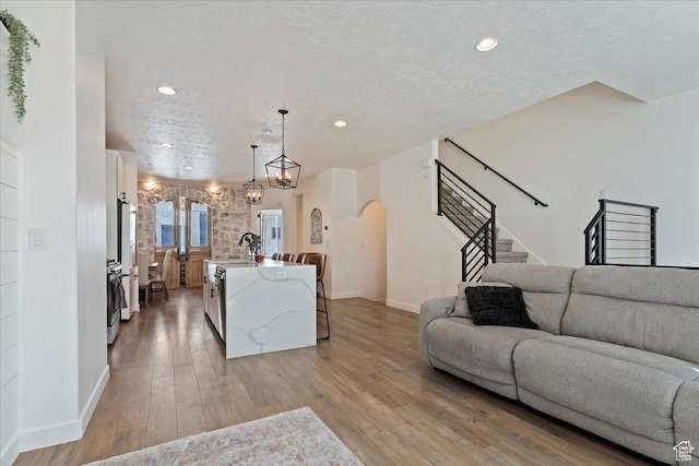 living room featuring arched walkways, a textured ceiling, recessed lighting, stairs, and light wood finished floors