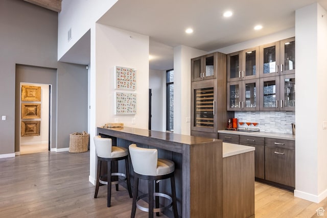 6379 W Golden Bear Loop, Park City, UT 84098 - kitchen with light wood-style floors, glass insert cabinets, dark brown cabinets, a breakfast bar, and decorative backsplash