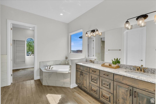 full bath featuring double vanity, wood finished floors, a sink, and a bath