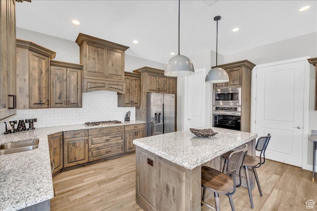 kitchen with a kitchen island, a sink, stainless steel appliances, light wood-type flooring, and backsplash