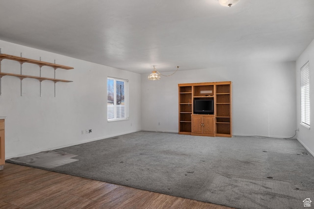 unfurnished living room with an inviting chandelier, carpet, baseboards, and wood finished floors