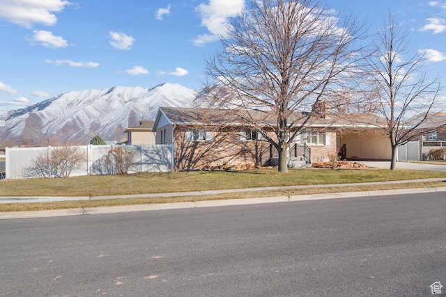 ranch-style home featuring driveway, fence, a mountain view, and a front yard