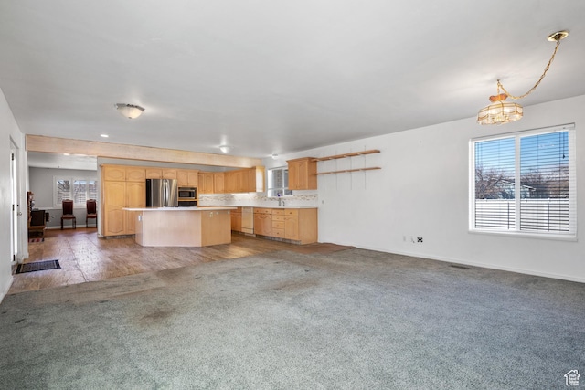 kitchen featuring light brown cabinetry, appliances with stainless steel finishes, light colored carpet, and a center island
