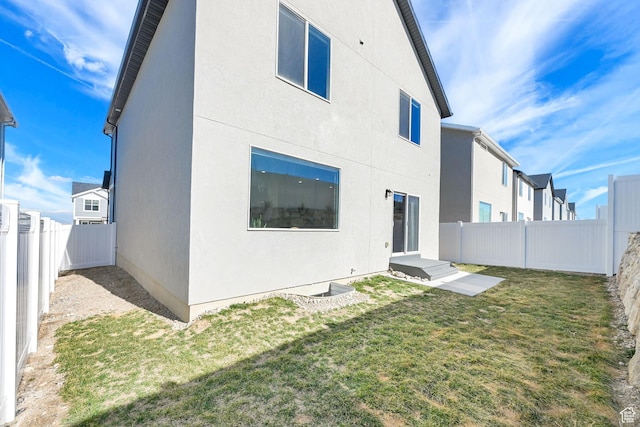 back of house featuring a fenced backyard, stucco siding, and a lawn