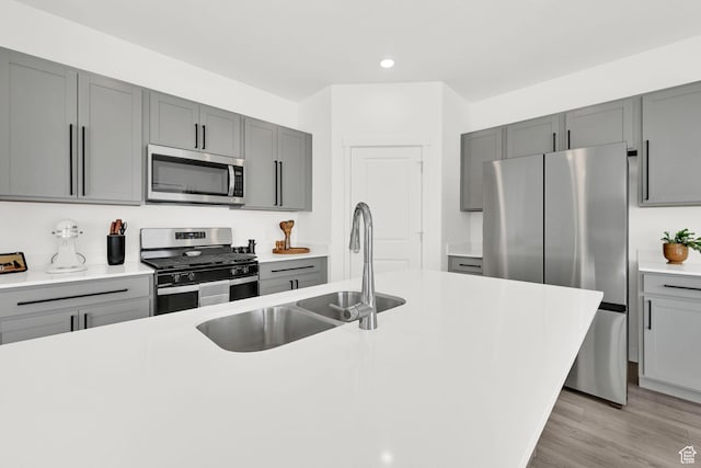 kitchen featuring light countertops, stainless steel appliances, gray cabinetry, a sink, and light wood-style floors