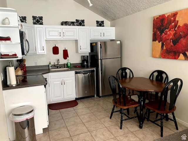 kitchen with stainless steel appliances, dark countertops, white cabinetry, and a sink