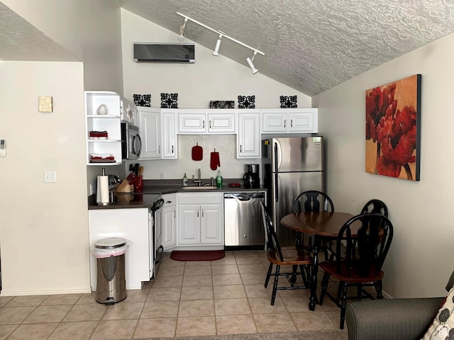 kitchen with a textured ceiling, light tile patterned flooring, vaulted ceiling, appliances with stainless steel finishes, and dark countertops