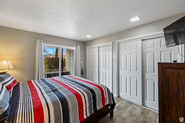 bedroom with a textured ceiling, wood finished floors, and two closets