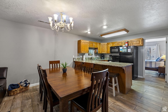 dining room with visible vents, light wood-style floors, a textured ceiling, a chandelier, and baseboards