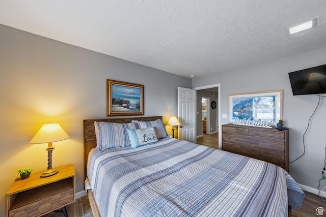 bedroom featuring a textured ceiling, baseboards, and wood finished floors
