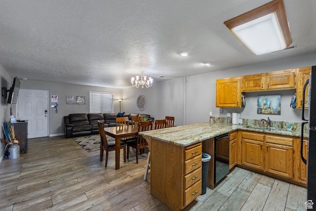kitchen featuring light stone counters, a notable chandelier, light wood-style floors, open floor plan, and a peninsula