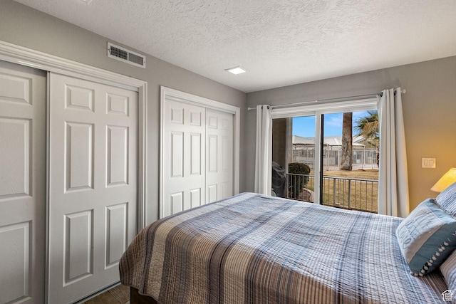 bedroom featuring a textured ceiling, multiple closets, visible vents, and access to exterior
