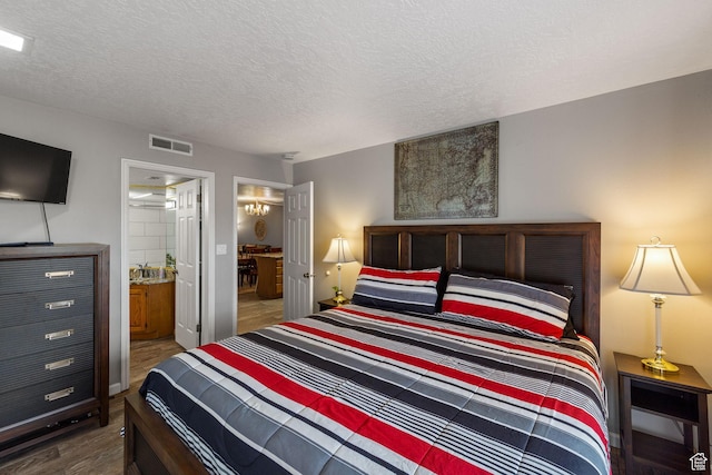 bedroom with a textured ceiling, dark wood finished floors, visible vents, and ensuite bathroom