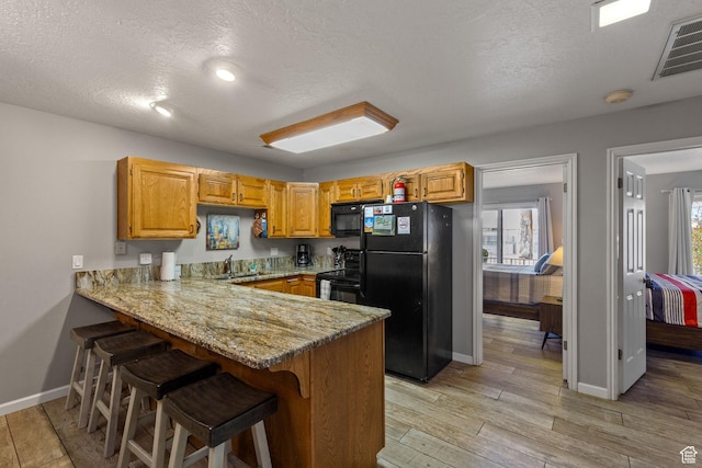kitchen featuring visible vents, a peninsula, light stone countertops, light wood-type flooring, and black appliances