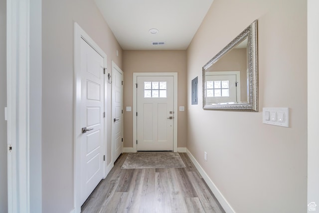 doorway featuring baseboards, light wood-style floors, visible vents, and electric panel
