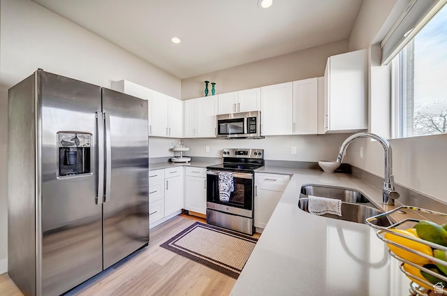 kitchen featuring light wood-style flooring, white cabinetry, stainless steel appliances, and a sink