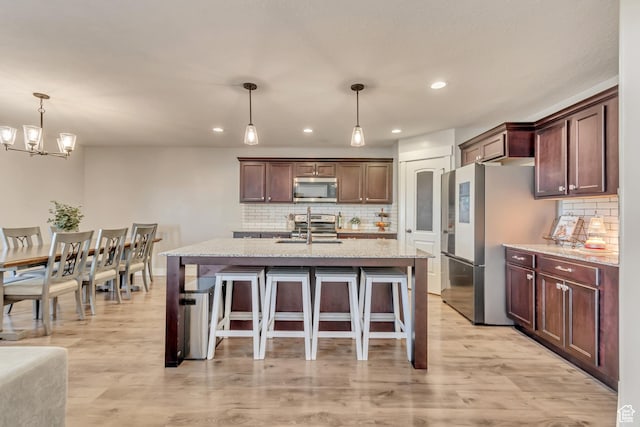 kitchen featuring a breakfast bar area, hanging light fixtures, stainless steel appliances, light wood-type flooring, and a sink