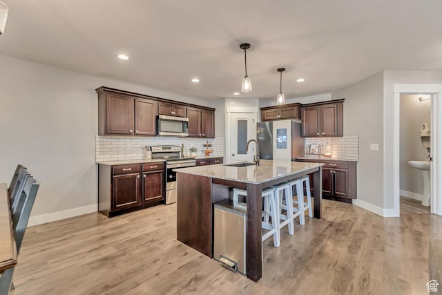 kitchen with stainless steel appliances, a sink, dark brown cabinets, light wood-type flooring, and a kitchen bar