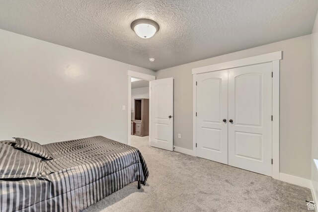 bedroom with baseboards, a closet, a textured ceiling, and light colored carpet