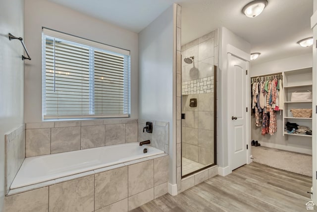 full bath featuring a bath, a stall shower, wood finished floors, and a walk in closet
