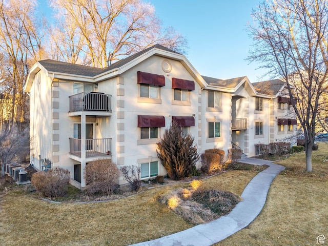 view of front of house with central air condition unit, a front yard, a balcony, and stucco siding