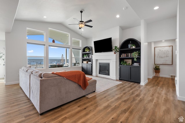 living room with built in shelves, wood finished floors, visible vents, baseboards, and a glass covered fireplace