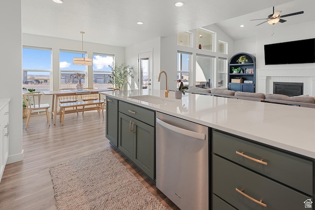 kitchen with dishwasher, a glass covered fireplace, light wood-style flooring, light countertops, and a sink