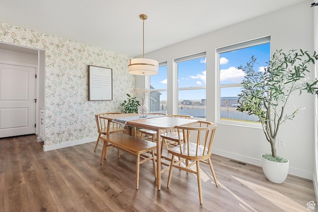 dining room featuring baseboards, wood finished floors, visible vents, and wallpapered walls