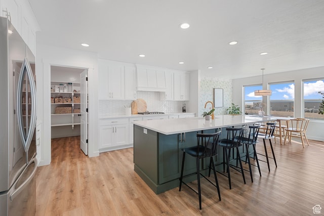 kitchen featuring white cabinets, appliances with stainless steel finishes, a kitchen island with sink, light countertops, and light wood-type flooring