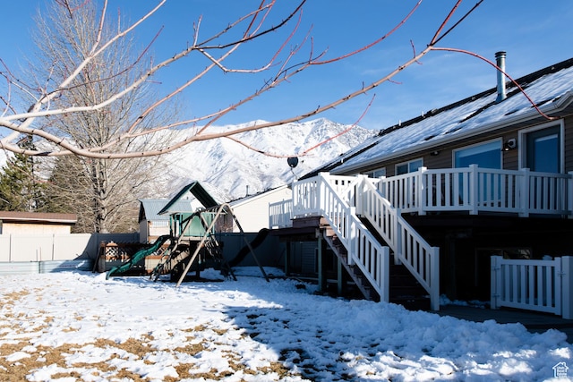 snow covered property with stairway, a playground, fence, and a deck with mountain view