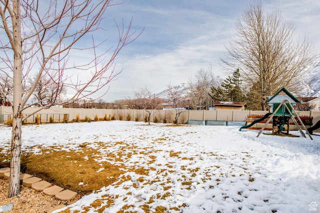 yard layered in snow featuring a fenced backyard and a playground